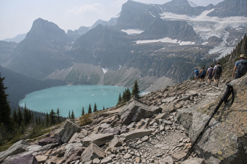 A guided hiking group on a gravel trail above a turquoise alpine lake