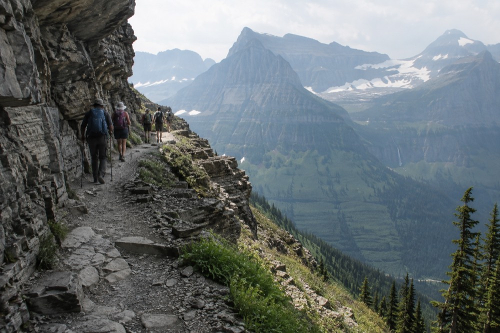 Hikers on a narrow alpine ridge trail with wide views of glaciated peaks