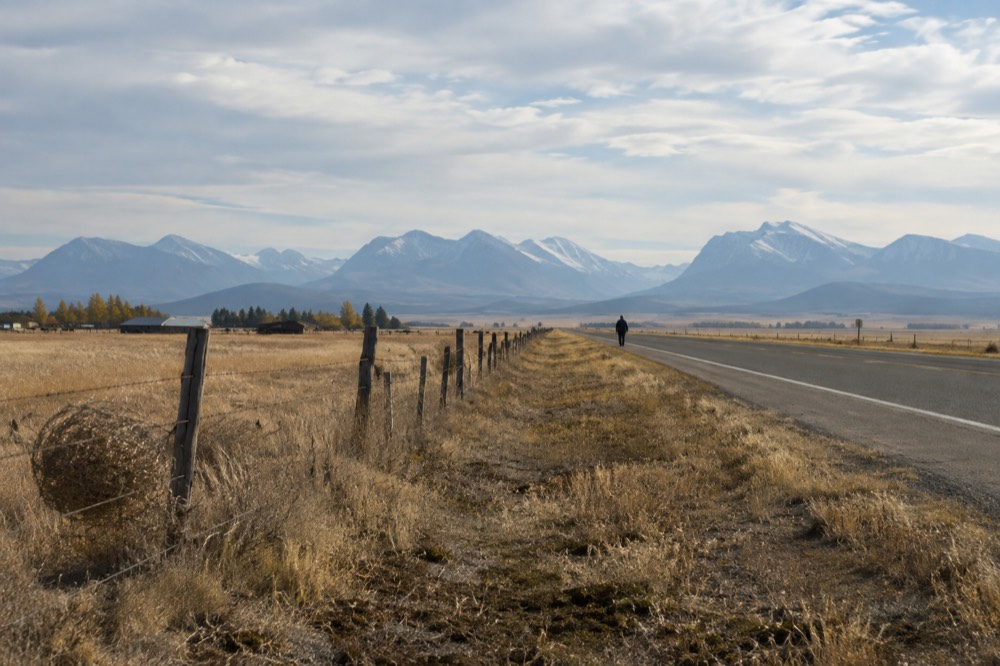 A long empty highway crossing rolling Montana grassland toward distant mountains