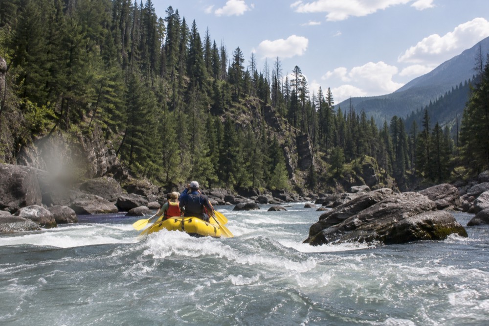 A raft floating through a rocky river canyon with forested slopes
