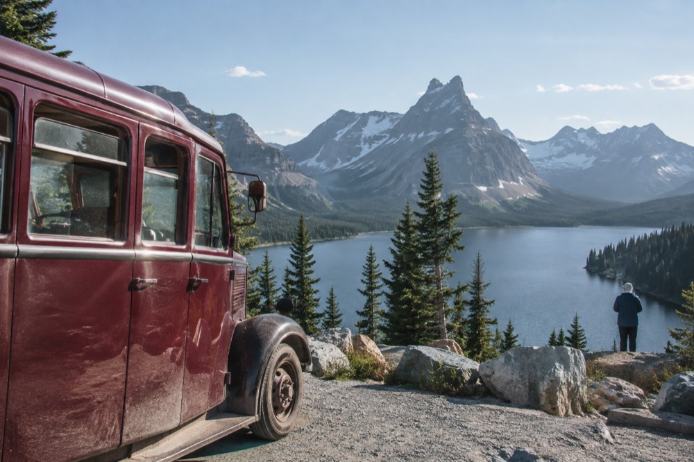 A red tour bus parked at a scenic overlook beside a mountain lake