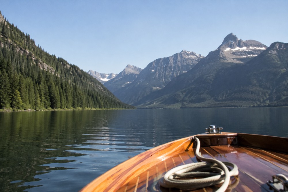 A wooden tour boat crossing a calm mountain lake toward a steep forested valley