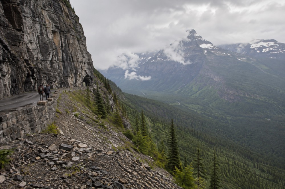A narrow mountain road hugging a cliff face high above a forested valley