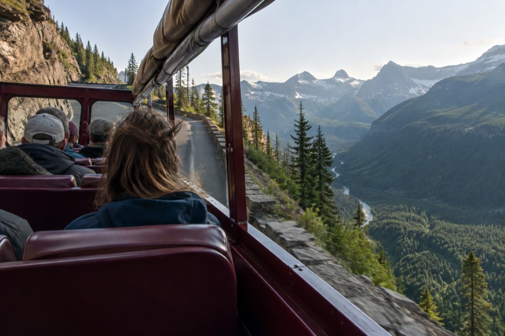 A red open-top touring bus traveling along a cliff-hugging mountain road above a valley