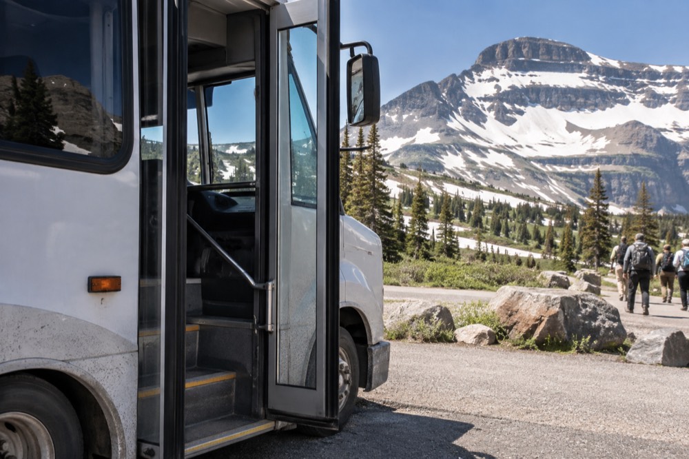A shuttle bus parked at a high mountain pass visitor center with peaks behind it