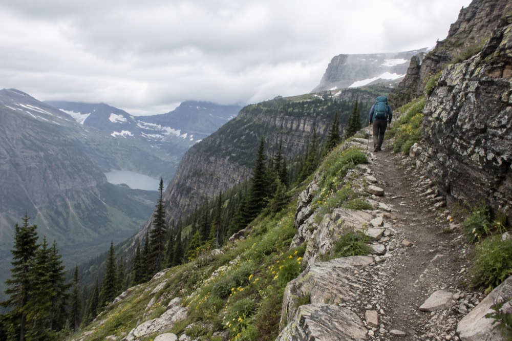 A hiker standing on a wide trail above a turquoise alpine lake at dawn