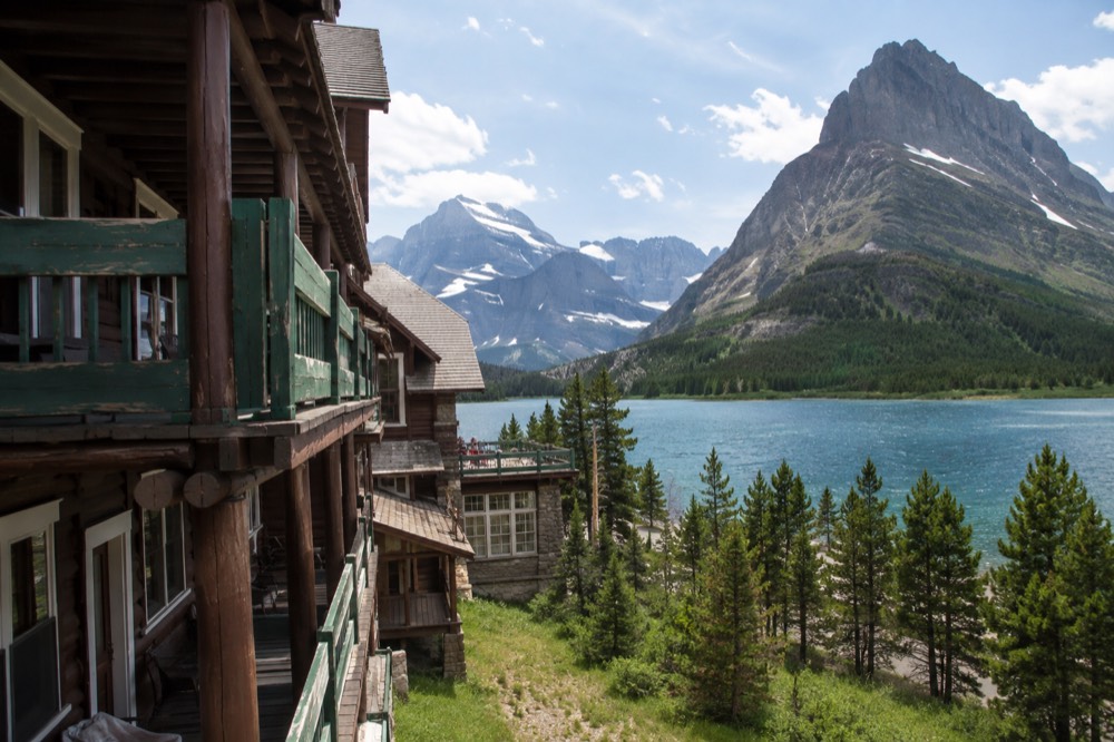 A wooden historic hotel beside a turquoise lake surrounded by tall mountains.