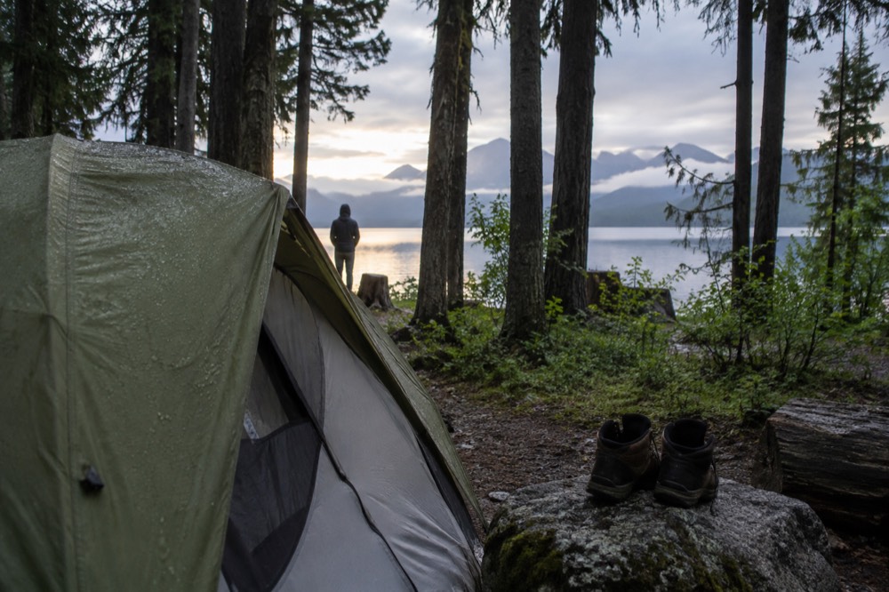A tent pitched in a forested campground with mountains rising behind the trees