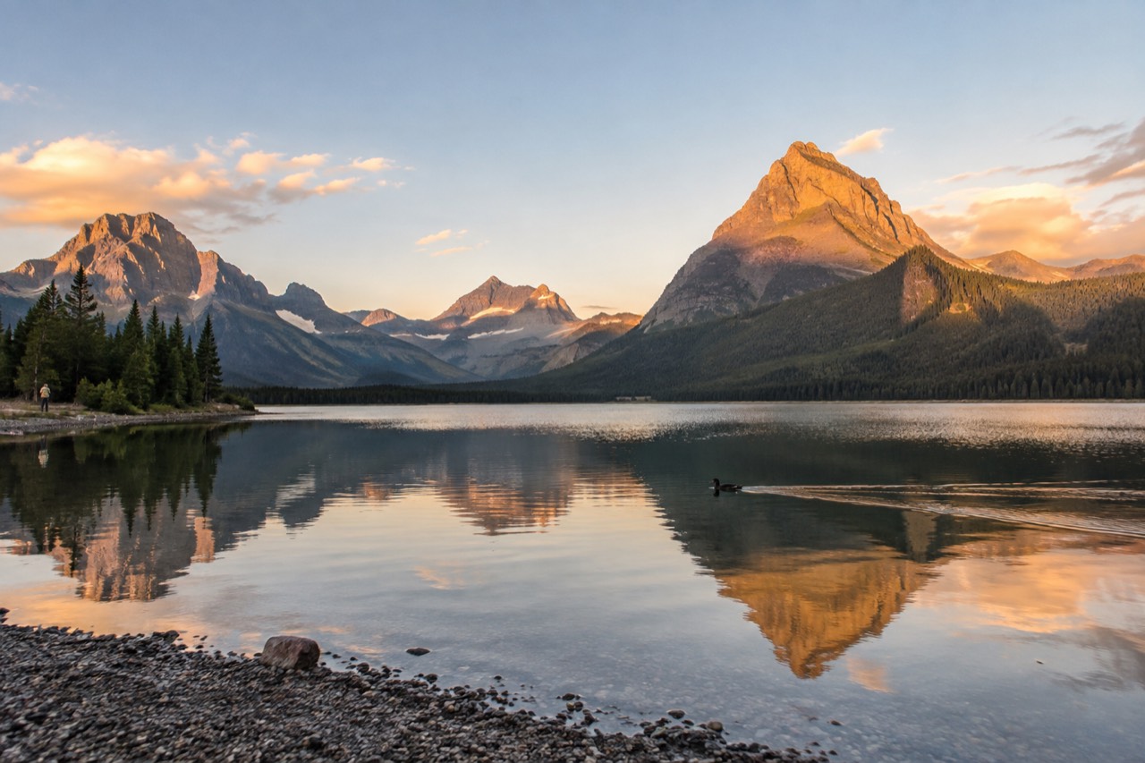 Mountain peaks reflected in a calm lake inside Glacier National Park at golden hour
