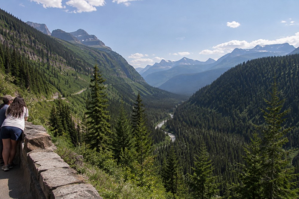 Aerial view of a winding road through a forested valley with mountains in the distance