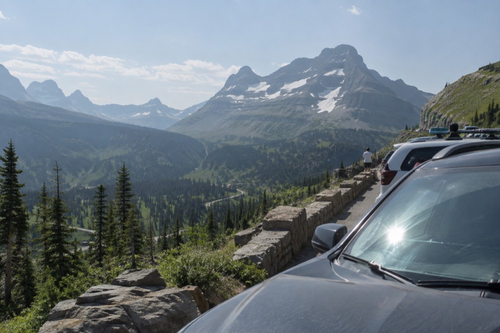 A winding mountain road with vehicles parked at a scenic overlook above a valley