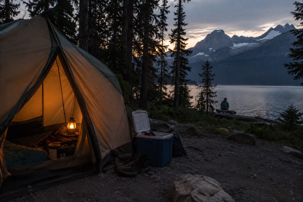 Tents pitched at a forested campground beside a lake at dusk
