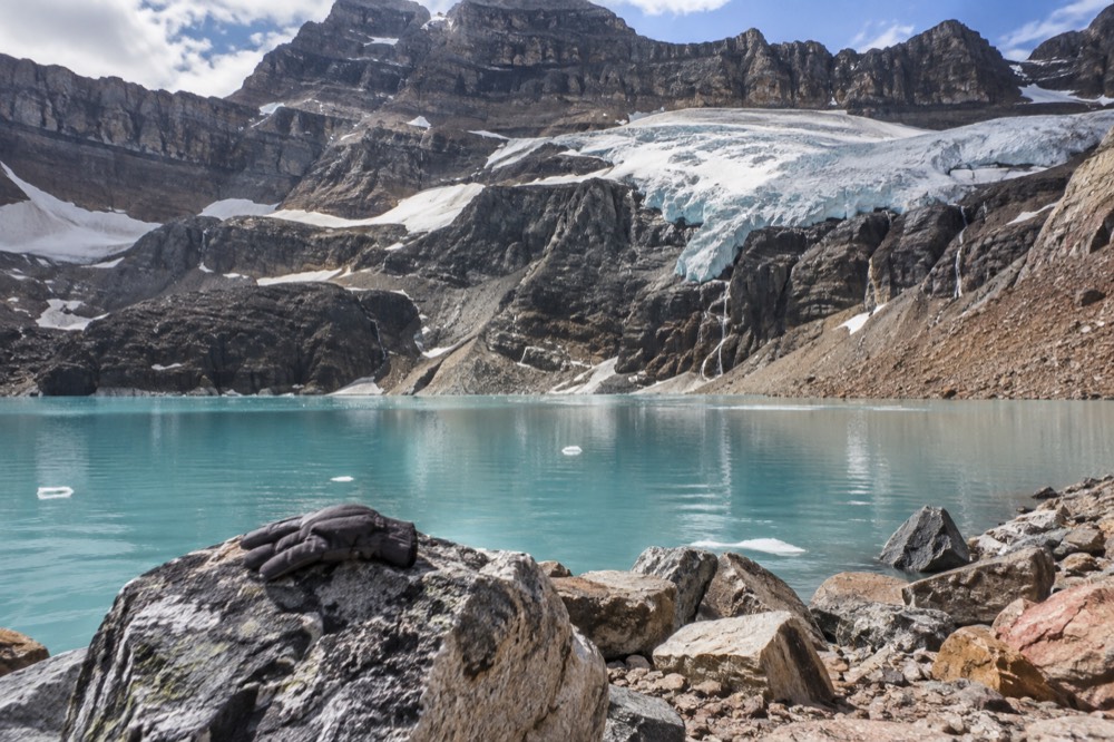 A turquoise alpine lake sitting below a hanging glacier on a rocky mountainside