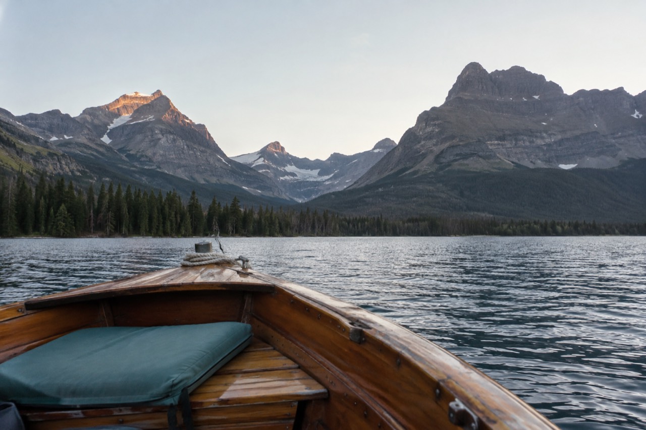A wooden tour boat crossing a calm mountain lake beneath tall peaks
