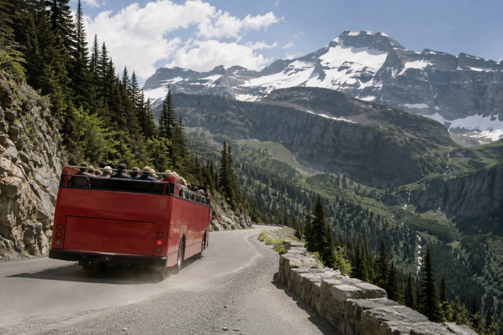 A red open-top touring bus winding along a mountain road with snowcapped peaks above