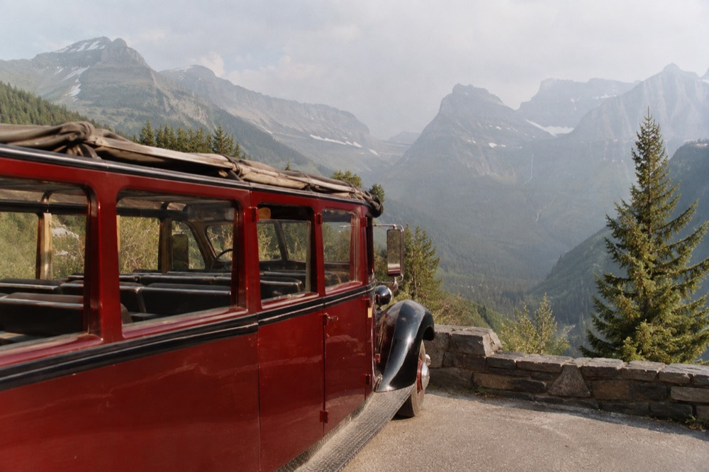 A red touring bus with its canvas top rolled back parked at a mountain overlook