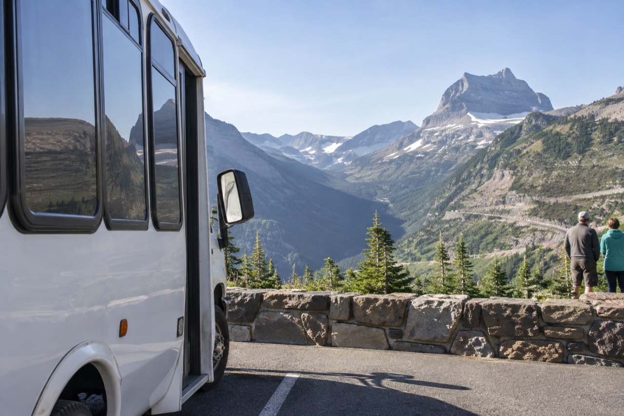A shuttle bus parked at a mountain overlook above a valley with a winding road