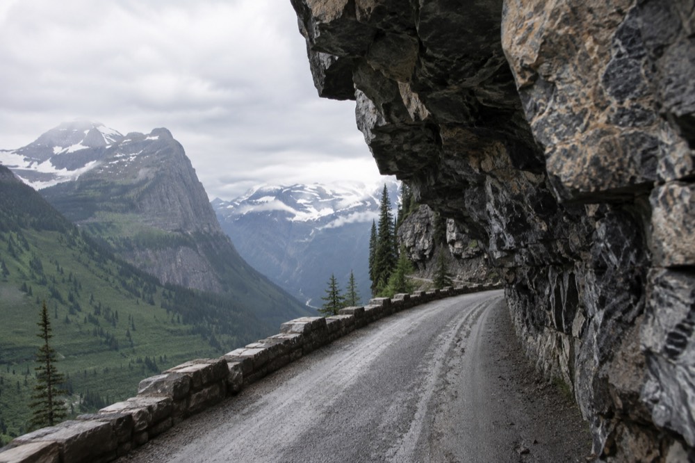 A narrow mountain road hugging a rock wall above a valley
