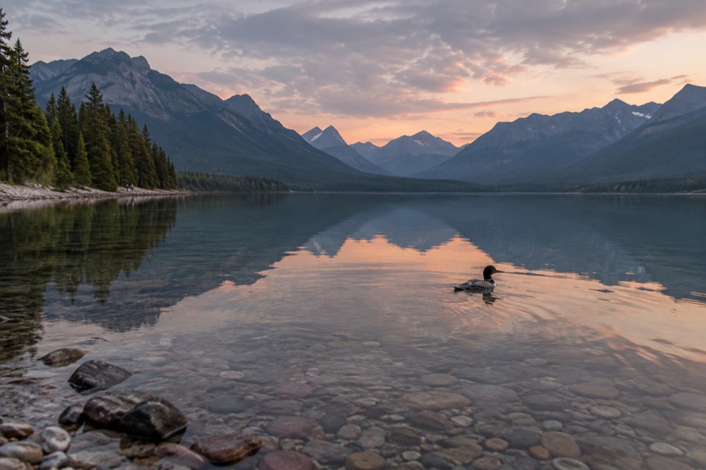 A calm mountain lake with a long valley and distant peaks reflected in still water