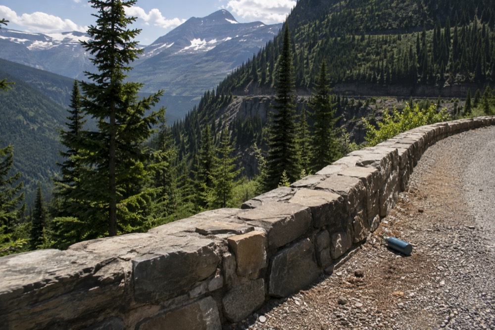 A winding mountain road with stone guard walls and forested slopes under a clear sky