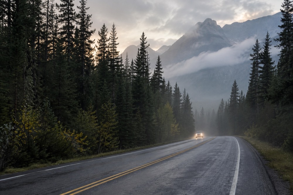 A quiet two-lane road curving toward forested mountains in early morning light