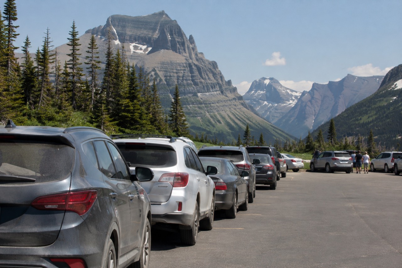 Logan Pass parking lot with mountains rising behind it under a clear summer sky