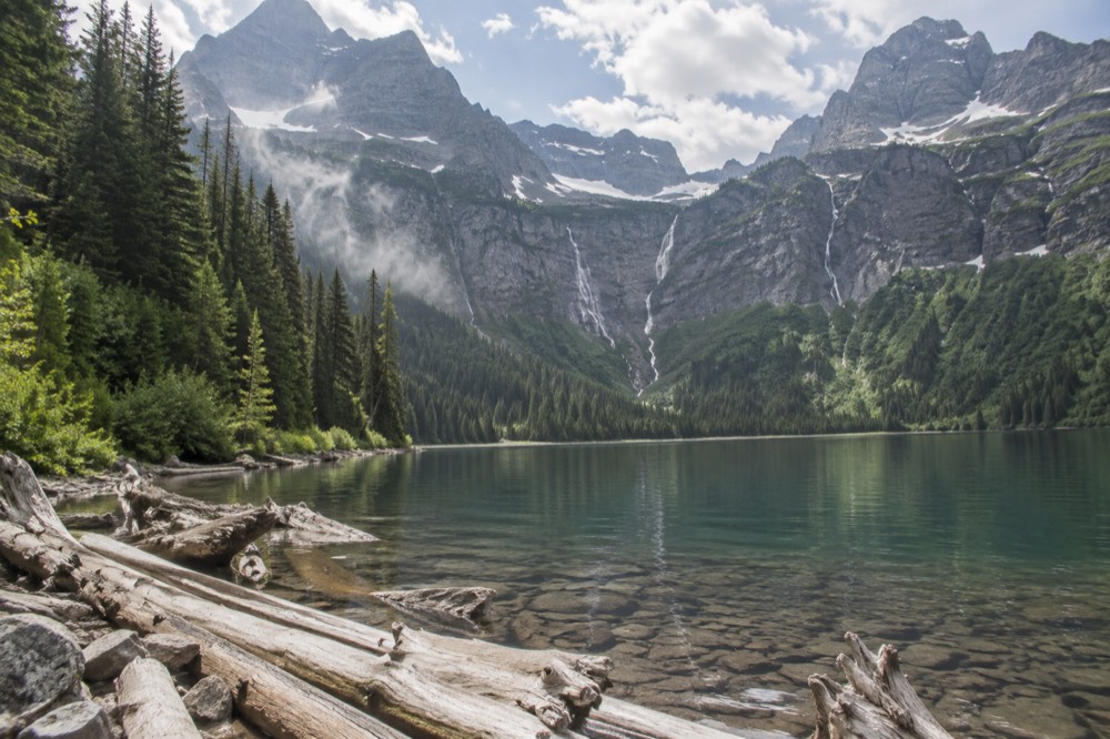 A calm mountain lake backed by tall waterfalls falling down a rock basin
