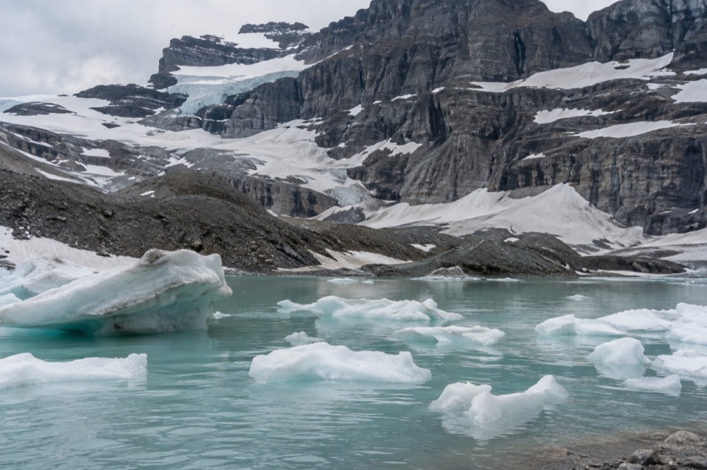 A turquoise alpine lake held in a bowl of steep cliffs with patches of snow on the ridges