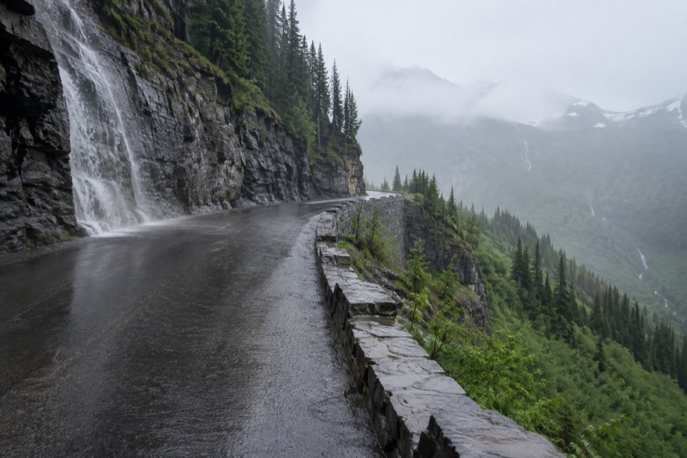 A winding mountain road climbing along a green hillside toward a high pass