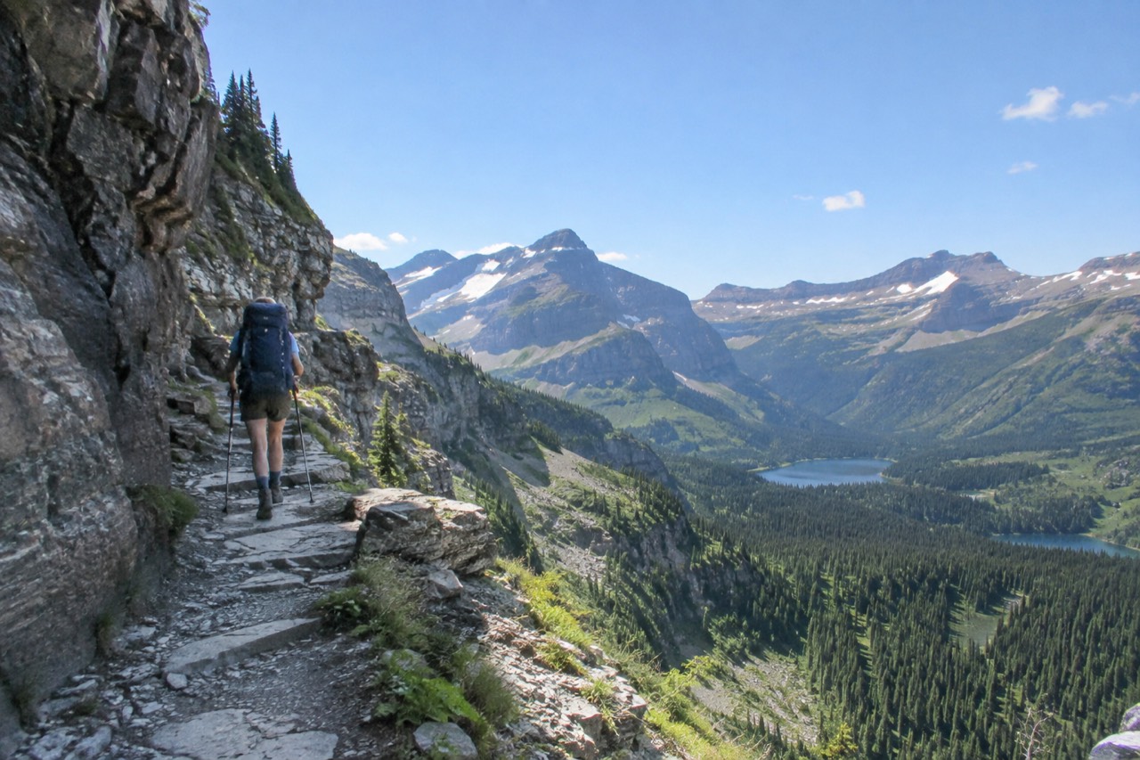 A hiker walking a high alpine trail above a valley of lakes and peaks in Glacier National Park