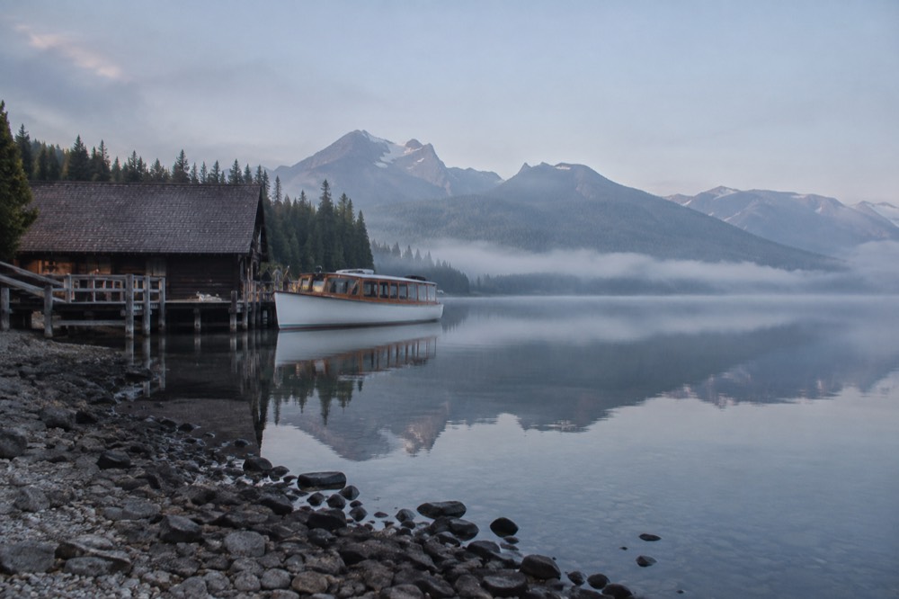 A long glacial lake with forested slopes and mountains reflected in still water