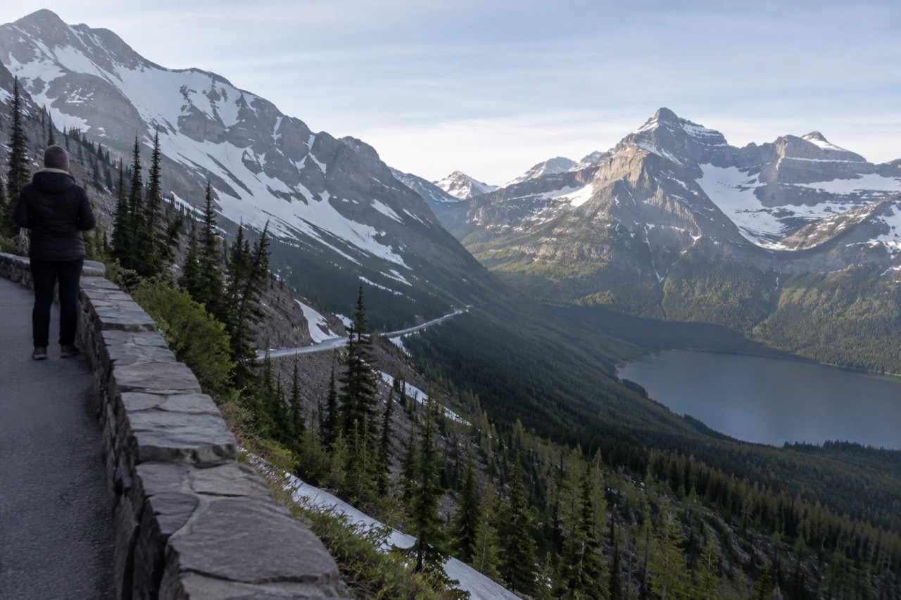 A winding mountain road with snowfields above a glacial lake and distant peaks