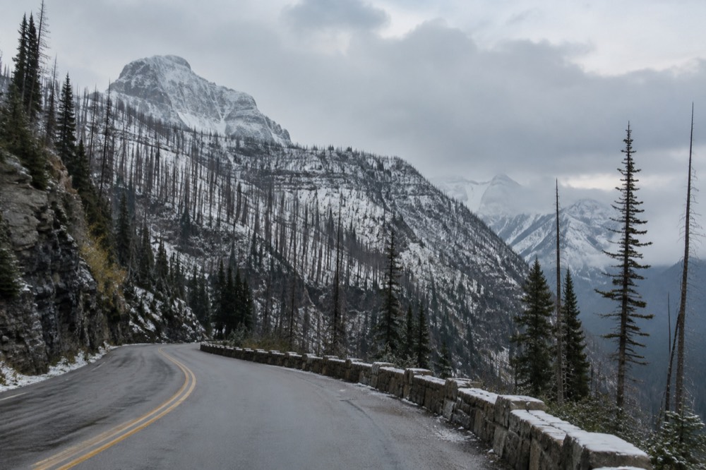 A winding mountain road climbing through forest toward a high pass