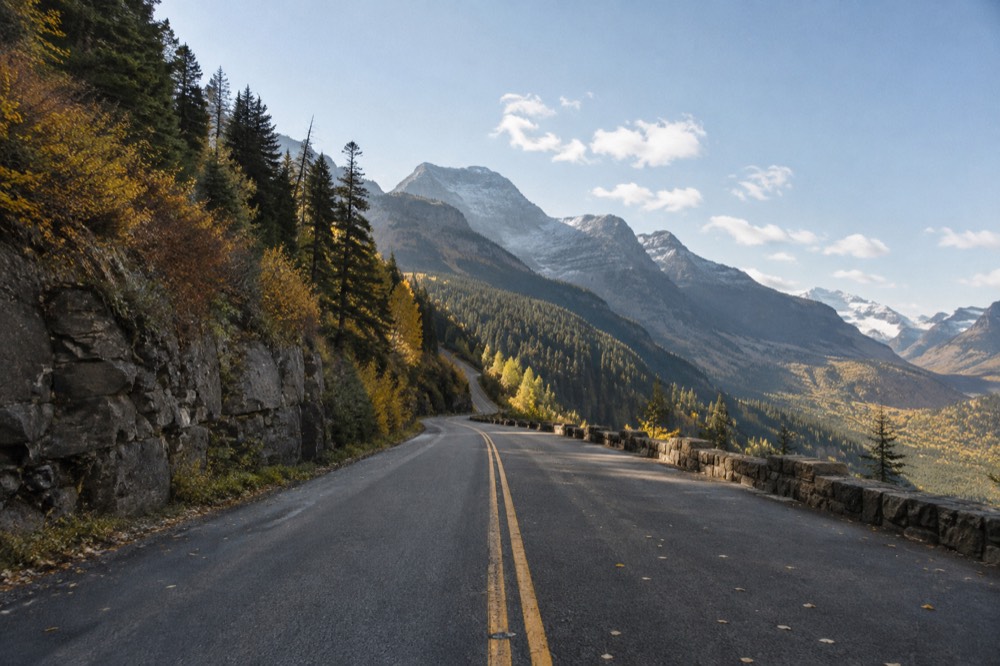An empty Going-to-the-Sun Road vista with golden autumn slopes and distant peaks