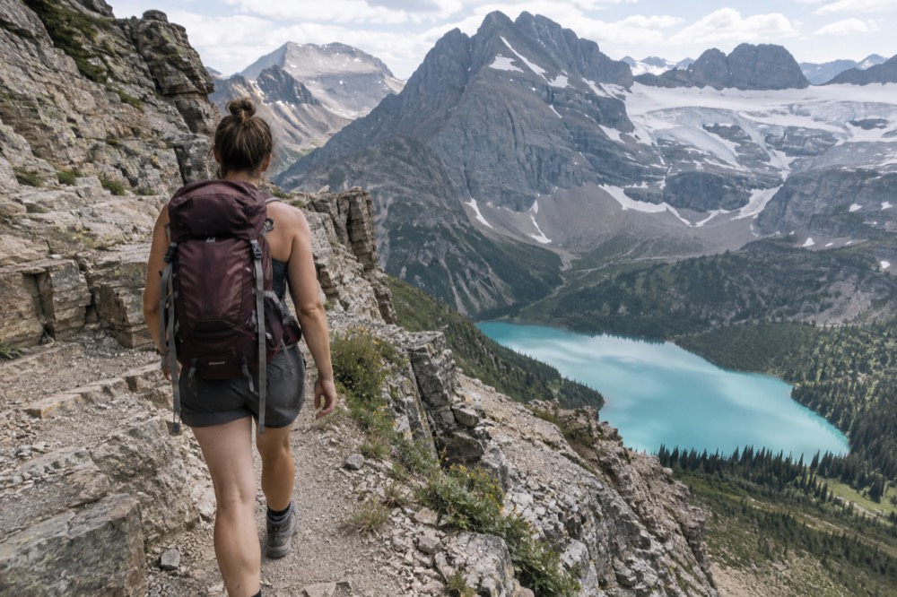 A hiker on a narrow trail above a turquoise alpine lake