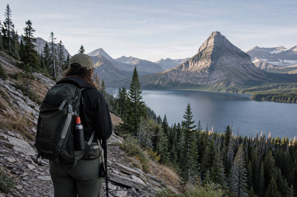 A hiker pausing on a rocky trail with a canister of bear spray clipped to a pack strap