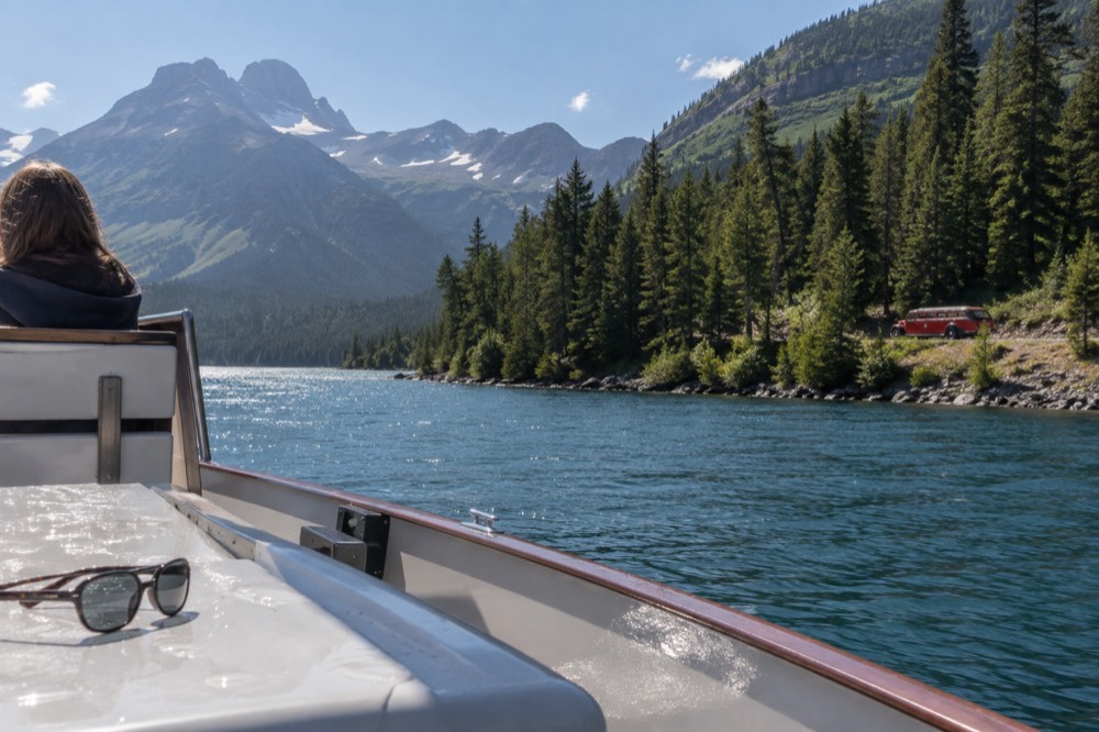 A red tour bus on a mountain road beside a glacial lake in Glacier National Park