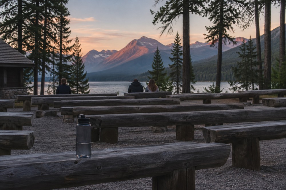 An outdoor stone amphitheater with log benches facing a mountain backdrop at dusk