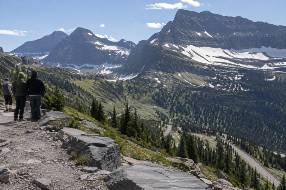 A winding mountain road climbing toward a high pass with snowfields along the ridgeline