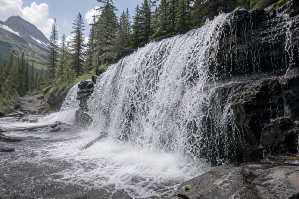 A wide waterfall spreading over a rock overhang into a plunge pool surrounded by forest
