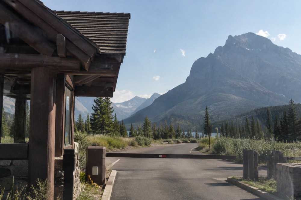 An entrance station sign at a park gateway with forested mountains behind it