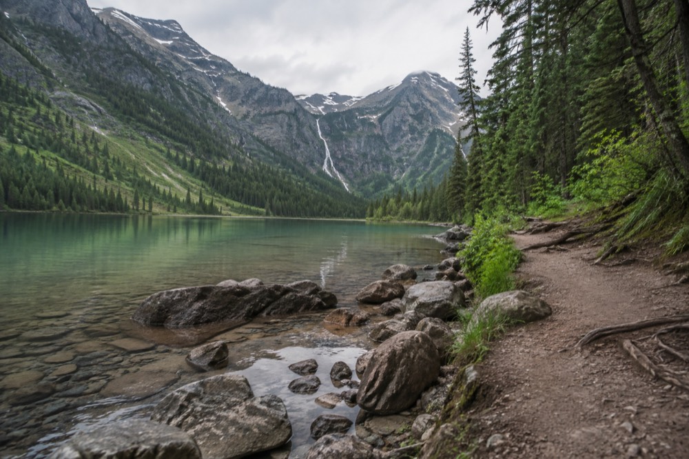 A hiker-free trail curving along a shoreline of an emerald green lake