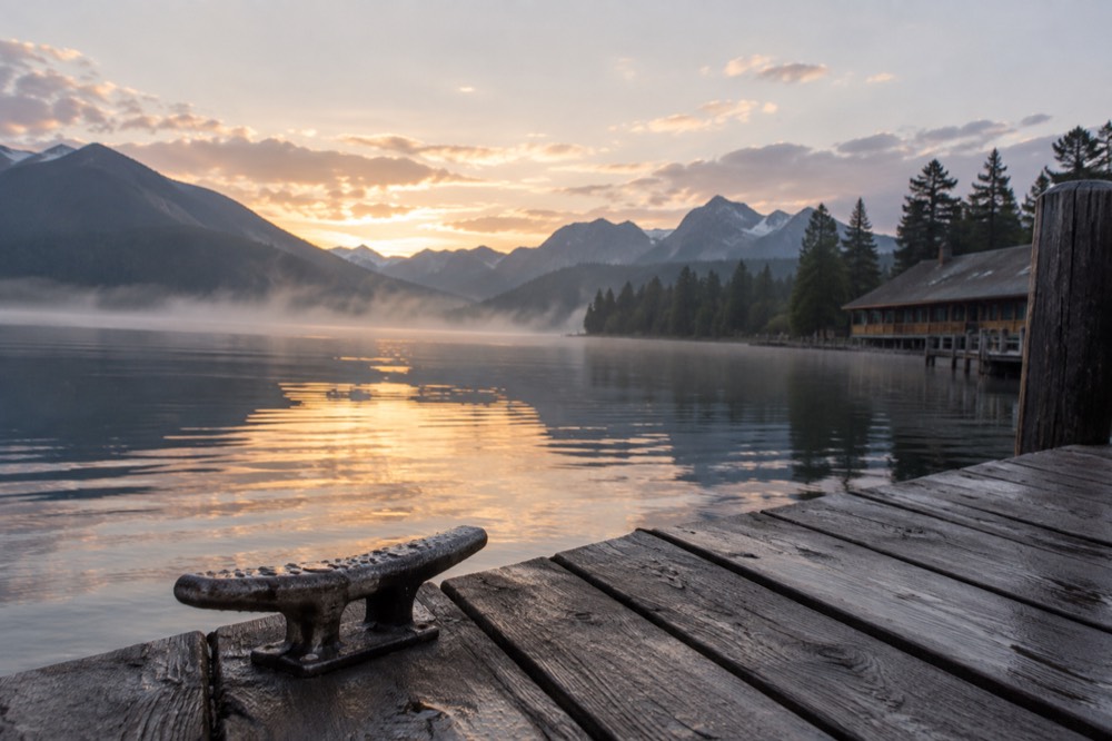 A wooden boat dock extending into a calm lake at sunrise with mist on the water
