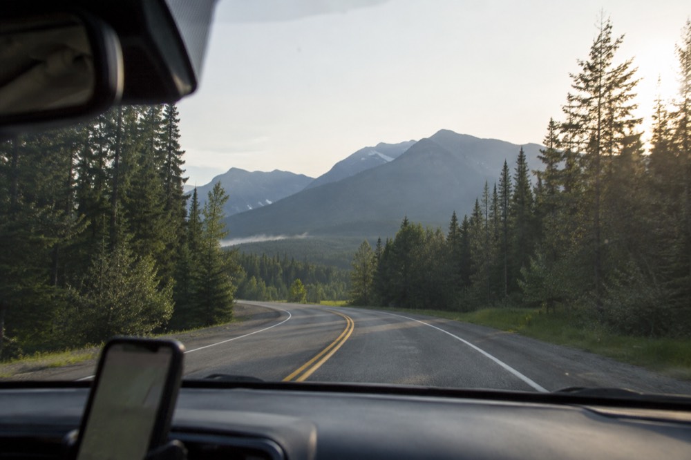 A car interior view through a windshield showing a mountain road curving toward a high pass