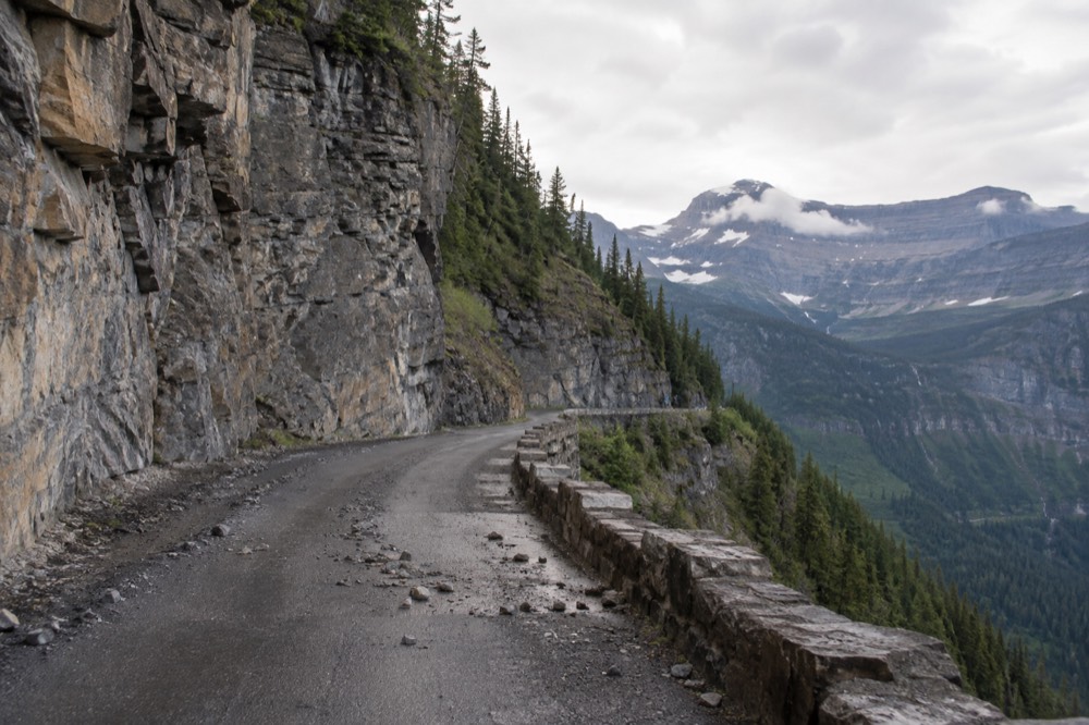 A narrow mountain road hugging a cliff face with a deep valley on the other side