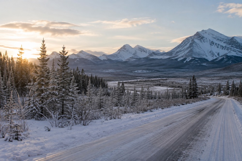 A snow-dusted valley road in winter with frosted evergreens and distant white peaks