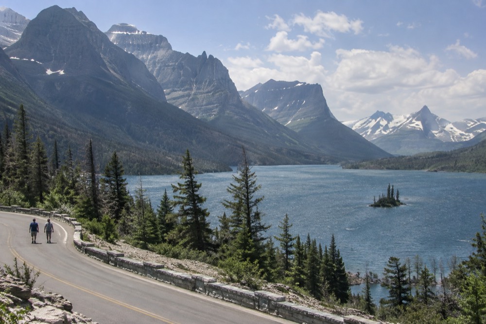 A winding mountain road descending toward a blue lake with a small forested island