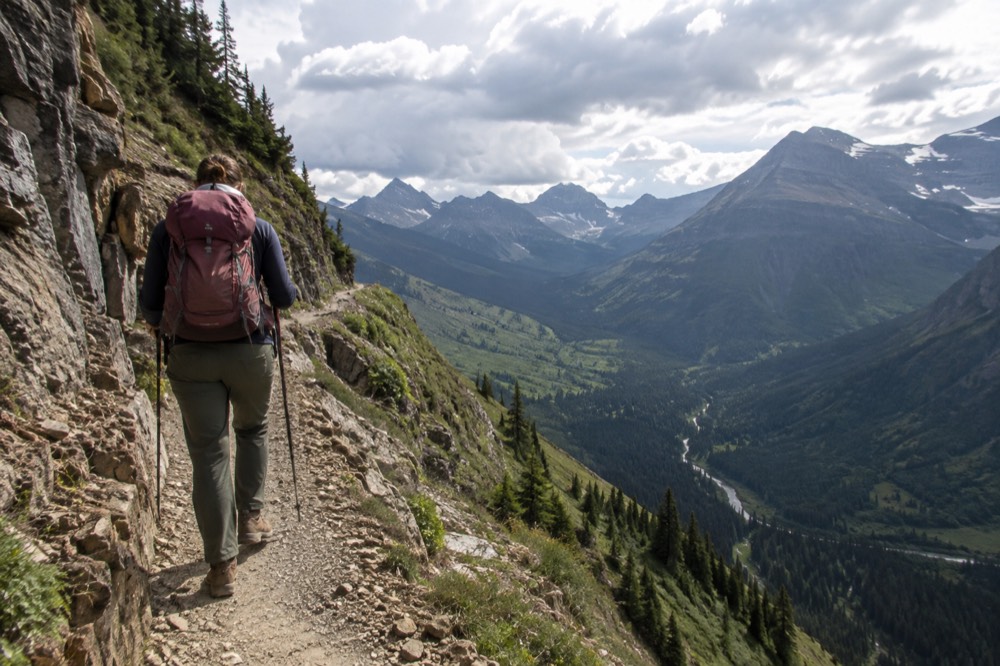 A hiker on a narrow trail along a green cliff face with a deep valley below