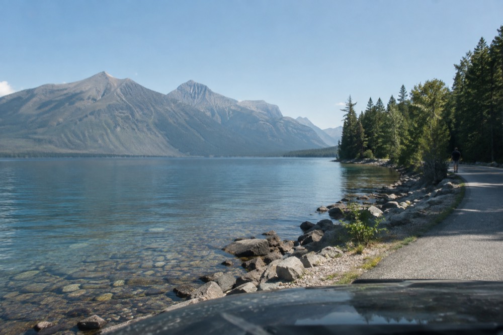 A scenic road curving along a turquoise lake inside Glacier National Park