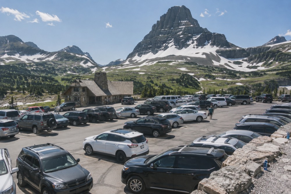 A full parking lot at a high mountain pass with a visitor center in the background
